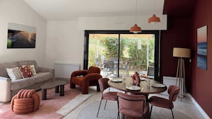 Un salon moderne avec un canapé, une table à manger pour quatre personnes et une grande fenêtre donnant sur l’extérieur.