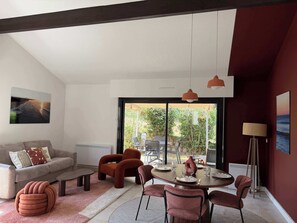 A modern living room with a sofa, a dining table set for four, and a large window offering a view of the outdoors. - T2 appartement 1 chambre, en RDJ avec terrasse (Anglet)