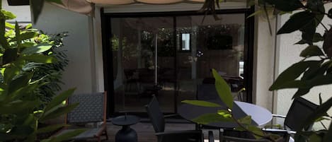 Een terras buiten met een overdekte zithoek, een tafel en stoelen.