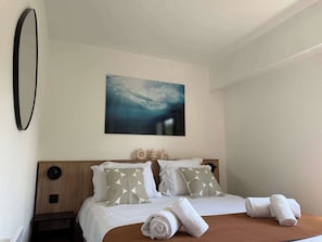 A hotel room with a bed, pillows, a painting, a bedside table, and towels. - T2 appartement 1 chambre, en RDJ avec terrasse (Anglet)