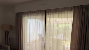 Une pièce dotée d’une grande fenêtre ornée de rideaux légers, d’un lampadaire, d’un canapé à rayures et d’un tapis à motifs.