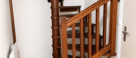 A wooden spiral staircase with a handrail and a door at the bottom.