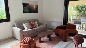 A modern living room with a sofa, armchairs, a coffee table, and a unique ottoman. - T3 appartement 2 chambres RDJ avec terrasse (Anglet)