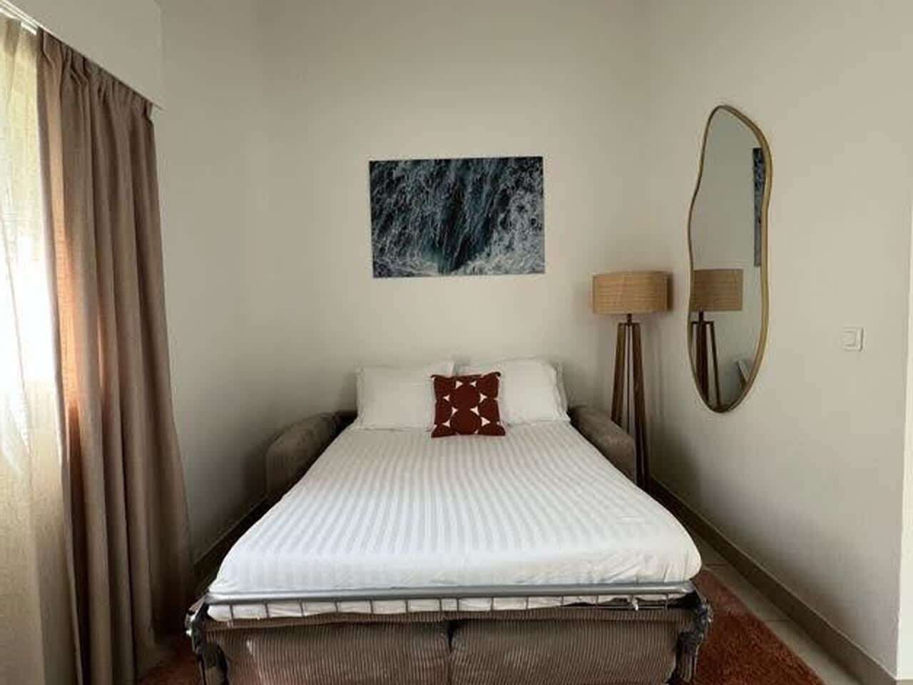 Quarto de hotel com cama, um quadro na parede, luminária e espelho.