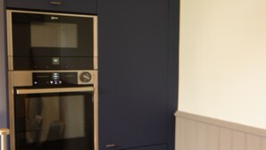 Una cocina con horno integrado y microondas, una mesa de comedor con sillas, y una bolsa de aperitivos.