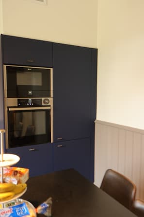 A kitchen with a built-in oven and microwave, a dining table with chairs, and a bag of snacks. - A Trip to the Canal (Moissac)