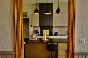 A modern kitchen with a central island, pendant lighting, and a view into the dining area through a doorway. - A Trip to the Canal (Moissac)