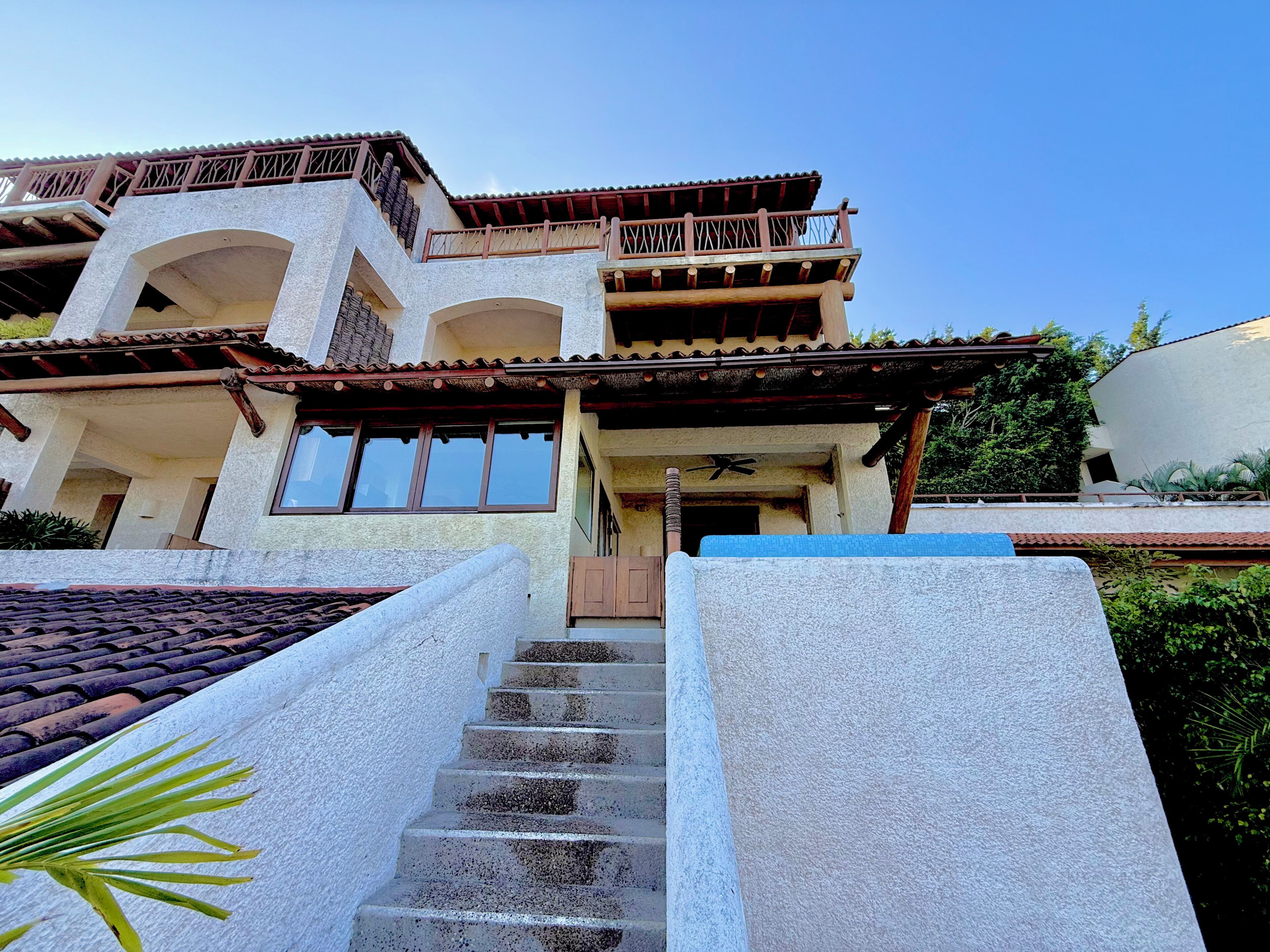 A multi-story building with a balcony, a staircase leading to the entrance, and a clear sky.