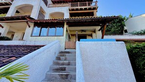 A multi-story building with a balcony, a staircase leading to the entrance, and a clear sky. - Vista Coral • Beachfront Condo • Jacuzzi & Pool • Ixtapa-Zihuatanejo (Ixtapa Zihuatanejo)