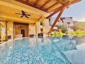 A clear view of an infinity pool with a ceiling fan, a door leading to a room, and a view of the surrounding buildings.