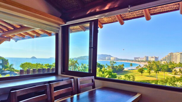 A dining area with a view of the ocean and cityscape. - Vista Coral • Beachfront Condo • Jacuzzi & Pool • Ixtapa-Zihuatanejo (Ixtapa Zihuatanejo)