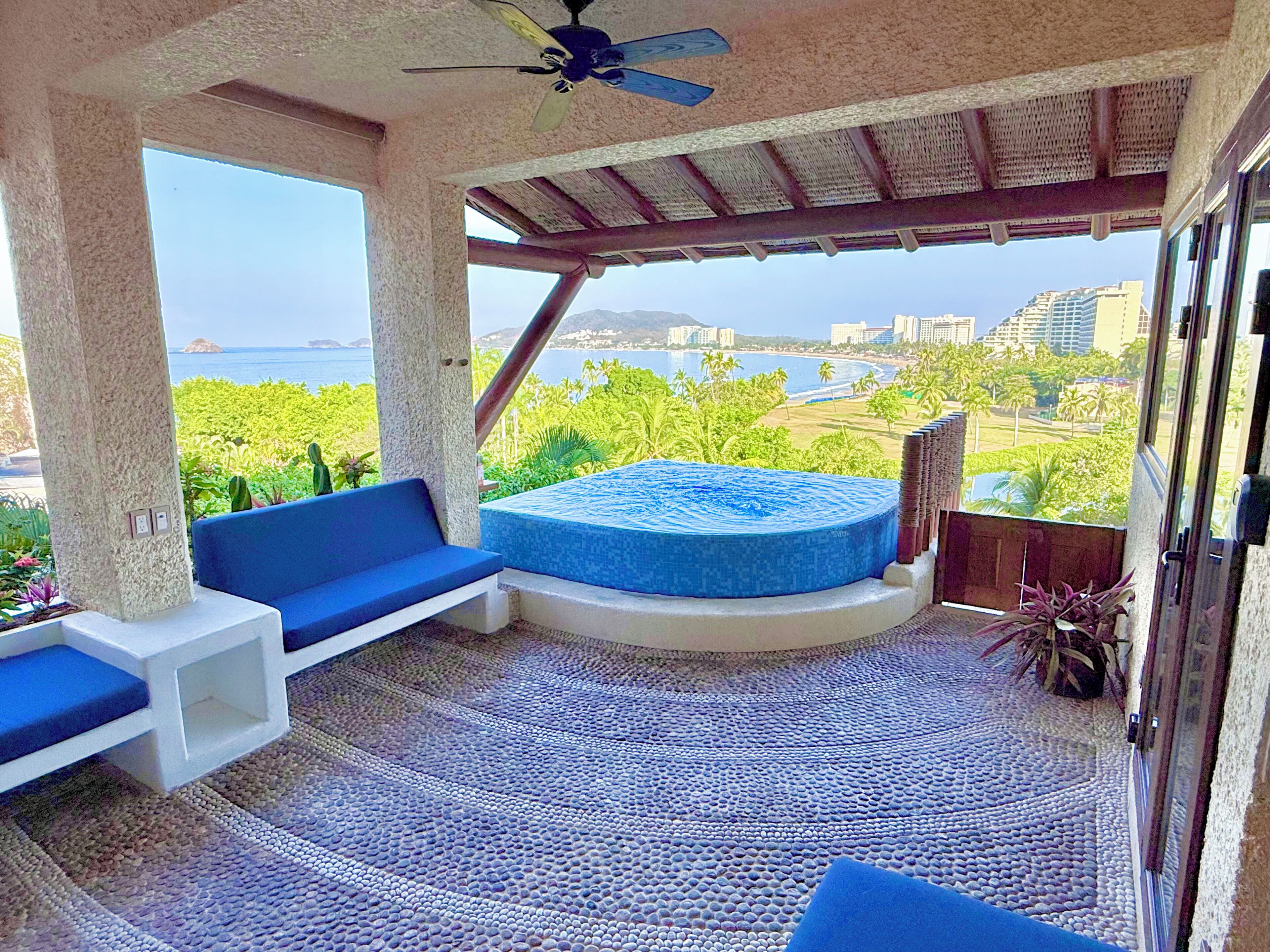 A balcony with a seating area, a hot tub, and a view of the ocean and cityscape.