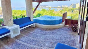 A balcony with a seating area, a hot tub, and a view of the ocean and cityscape. - Vista Coral • Beachfront Condo • Jacuzzi & Pool • Ixtapa-Zihuatanejo (Ixtapa Zihuatanejo)
