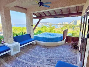 A balcony with a seating area, a hot tub, and a view of the ocean and cityscape.