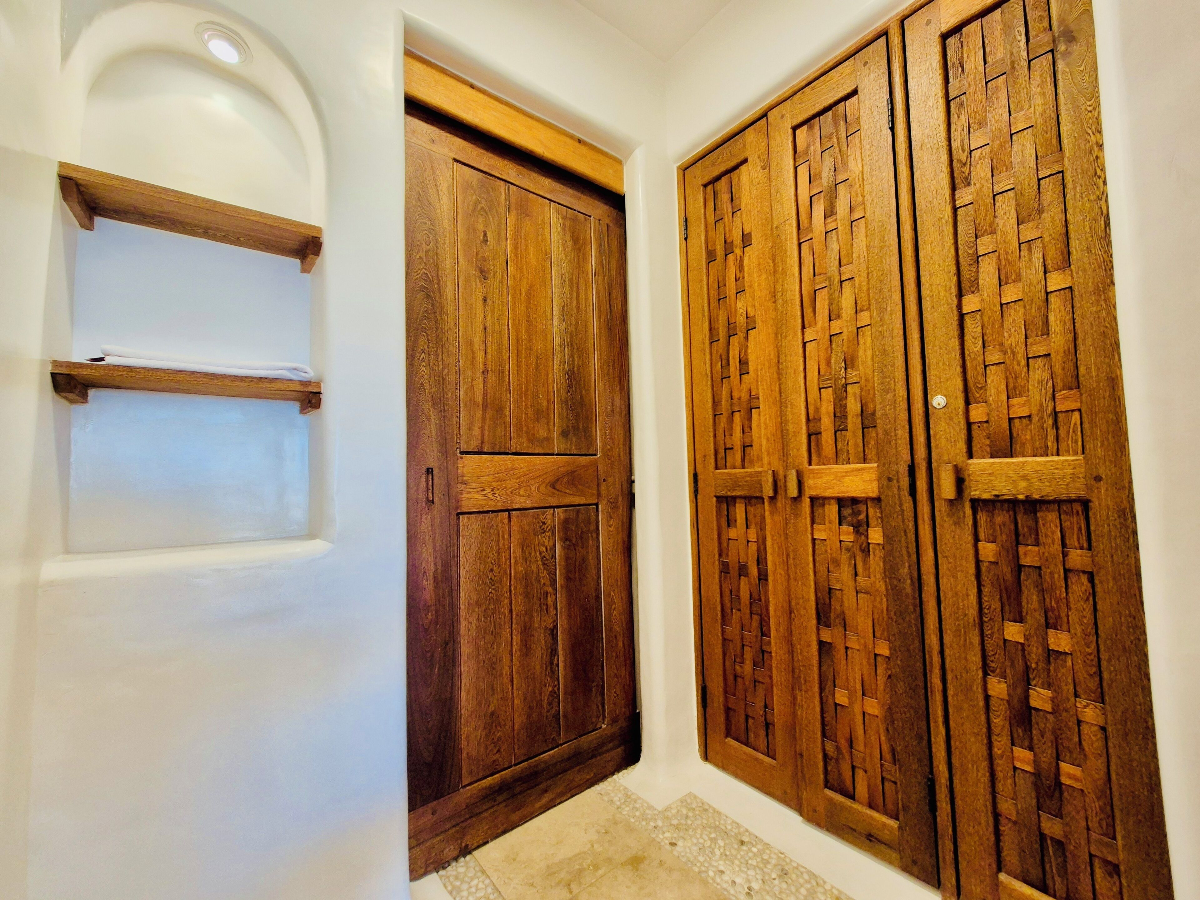 A hallway with a white wall, a wooden door with a simple design, and a wooden door with a lattice pattern.