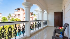 A balcony with white columns, a black metal railing, and a table with a vase of flowers.