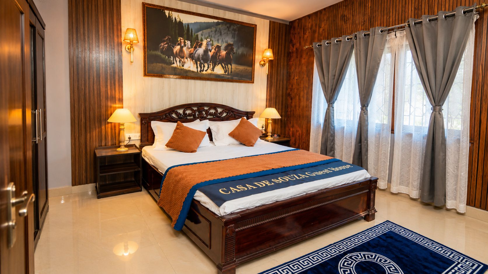 A hotel room with a wooden bed, two bedside tables with lamps, a large painting on the wall, and curtains on the windows.