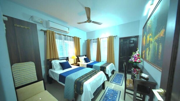 A hotel room with two beds, a ceiling fan, an air conditioning unit, a desk with a chair, and a painting on the wall. - Casa de Souza (Verna)