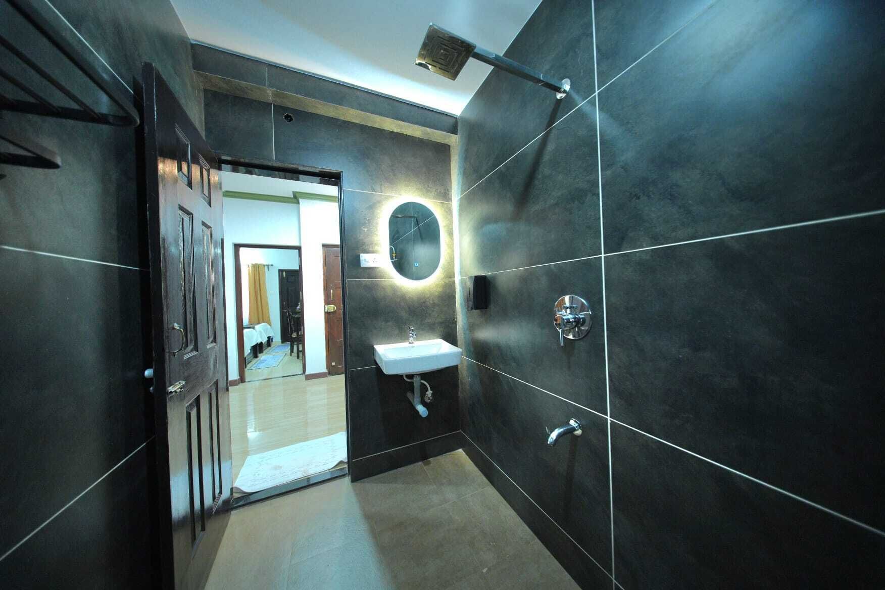 A modern bathroom with dark tiles, a round mirror, a sink, and a shower.