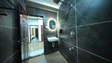 A modern bathroom with dark tiles, a round mirror, a sink, and a shower.