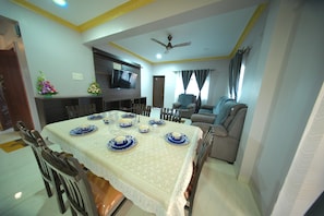A dining area with a table set for four, chairs, a television, and a sofa in the background.