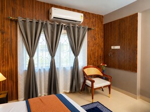Ein Hotelzimmer mit Bett, Stuhl, Wandklimaanlage und einem Vorhangfenster.