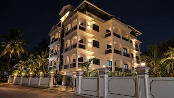 Um hotel com vários andares, varandas, portão fechado e palmeiras.