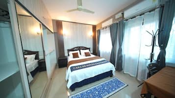 Ein Hotelzimmer mit Bett, Schreibtisch, Stuhl, Spiegel, Deckenventilator und Vorhängen.