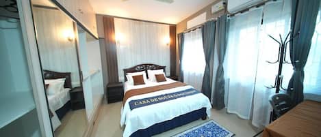 A hotel room with a bed, a desk, a chair, a mirror, a ceiling fan, and curtains.