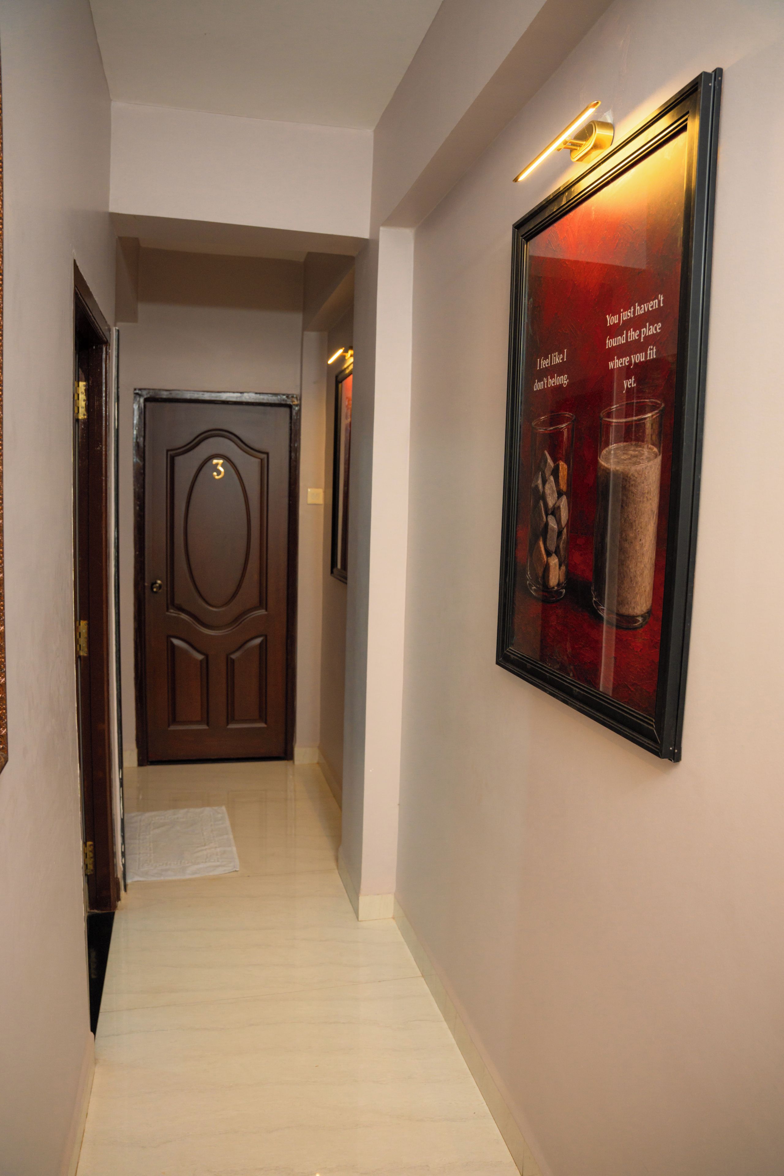 A hallway with a wooden door marked with the number 3, a framed picture on the wall, and a light fixture above it.