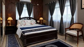 Una habitación de hotel con una cama, dos lámparas de noche, una silla y un ventanal con cortinas.