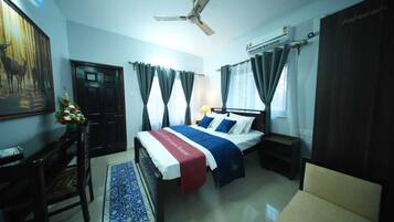 Ein Hotelzimmer mit Bett, Schreibtisch, Stuhl, Deckenventilator und einem Fenster mit Vorhängen.