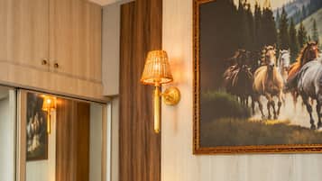 Luminária de parede com cúpula trançada, quadro com cavalos e painel de parede em madeira.
