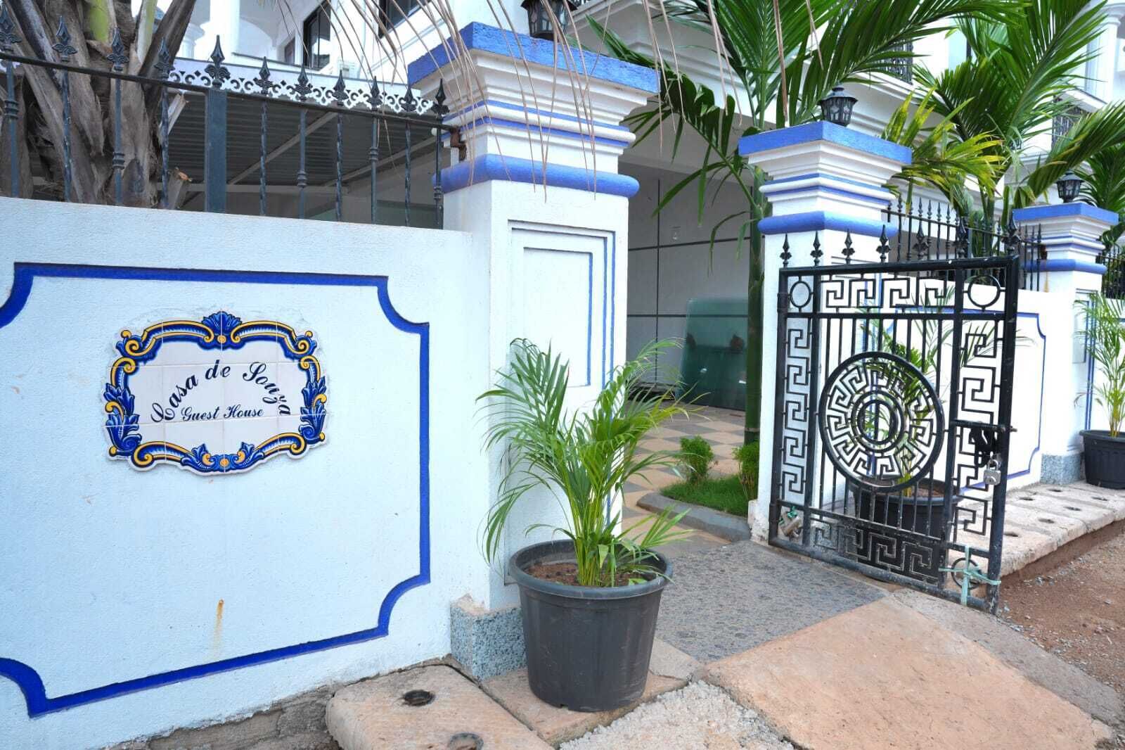 Une entrée fermée par un portail, agrémentée d’une enseigne décorative indiquant : « Casa de Souza, maison d’hôtes ».