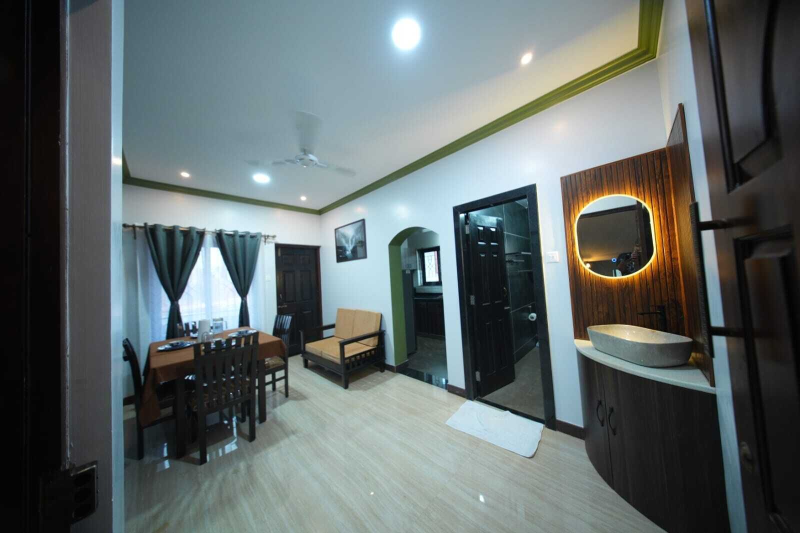 A living room with a dining area, a sofa, a ceiling fan, and a kitchen area with a sink and mirror.