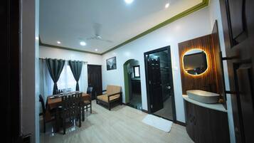 A living room with a dining area, a sofa, a ceiling fan, and a kitchen area with a sink and mirror.