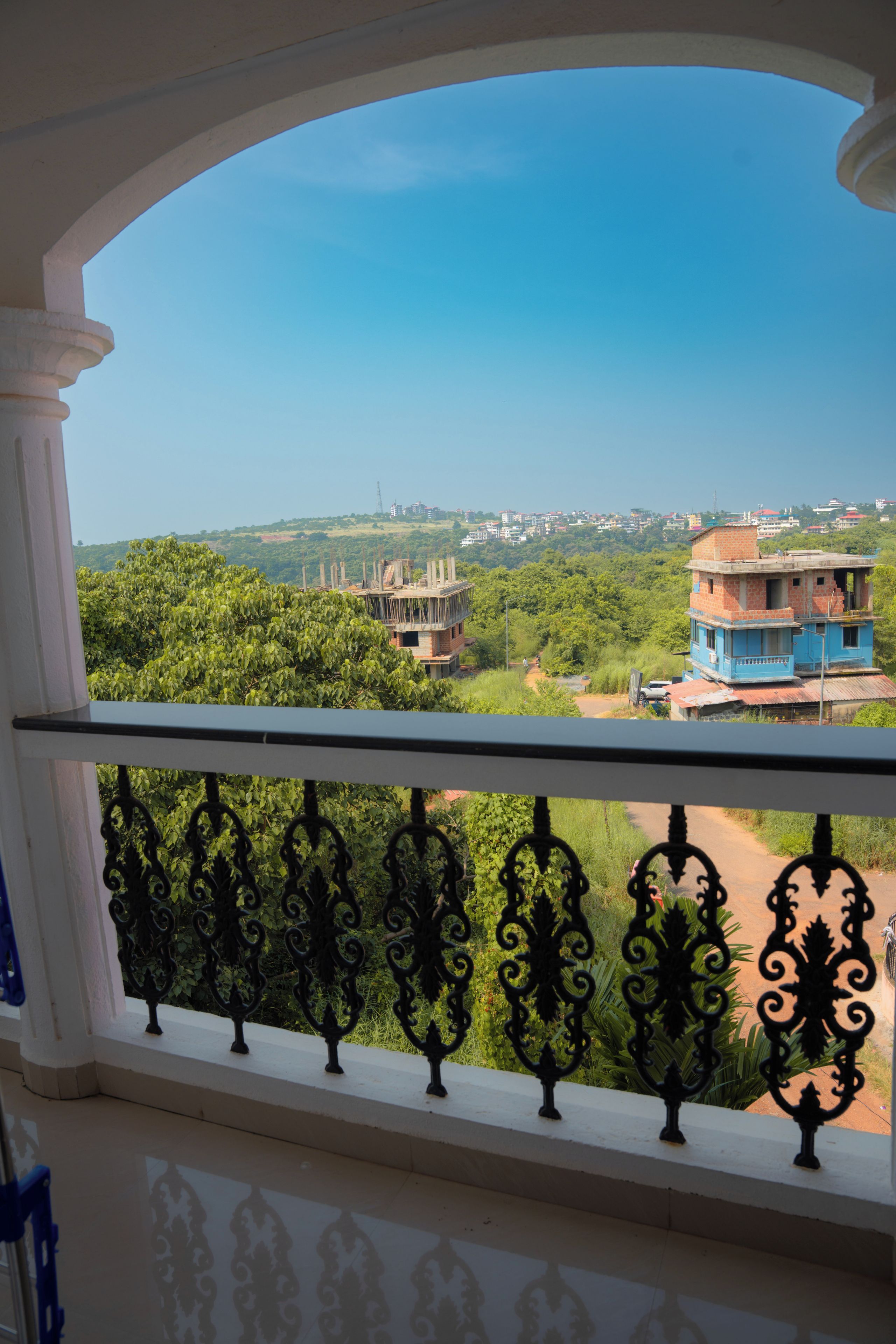 A balcony with ornate black railings and a view of a residential area with buildings and greenery.
