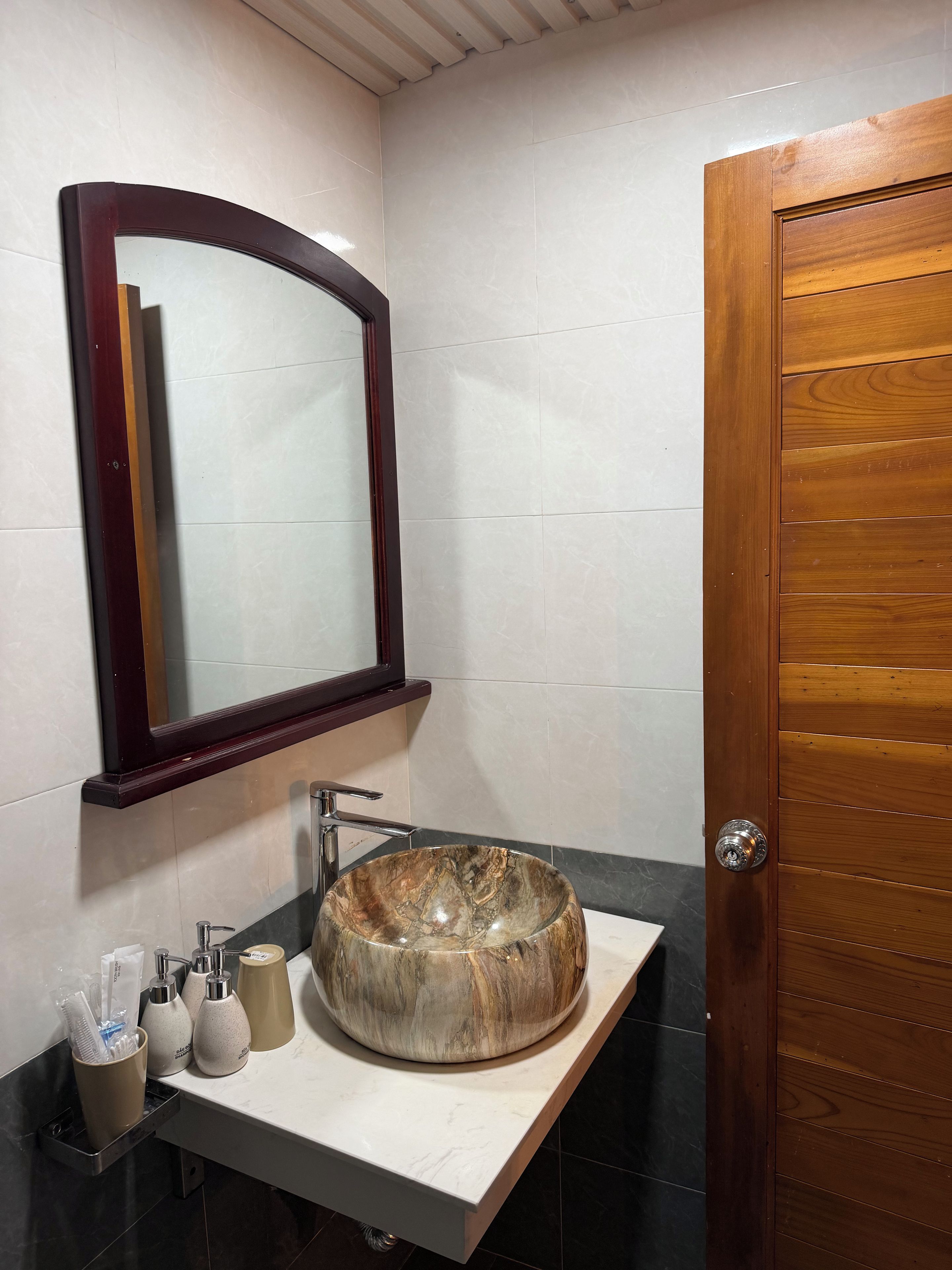 A bathroom with a marble sink, a wooden door, and a mirror with a dark frame.