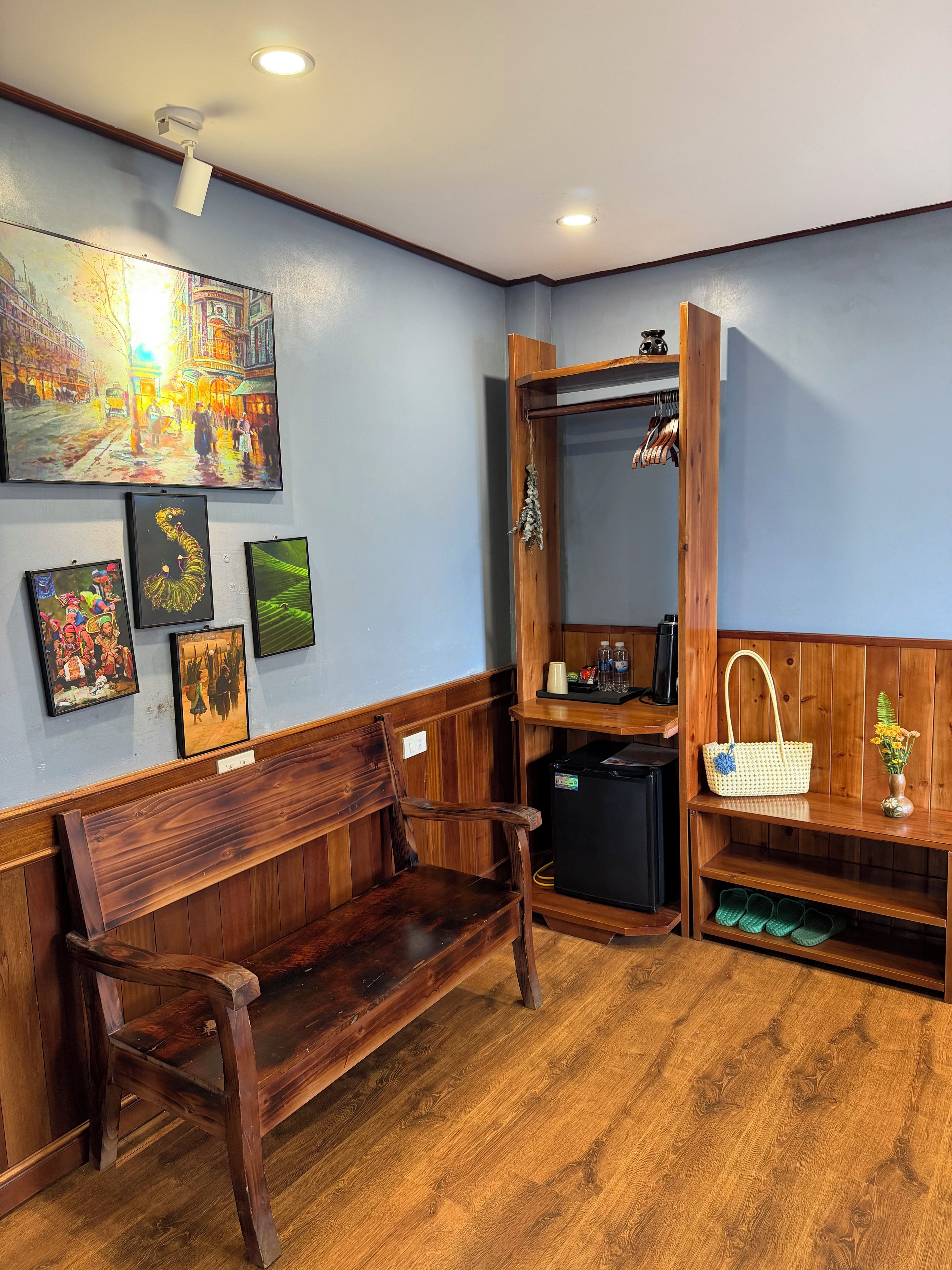 A room with a wooden bench, a wall-mounted mirror, a shelf with a handbag, and framed artwork.