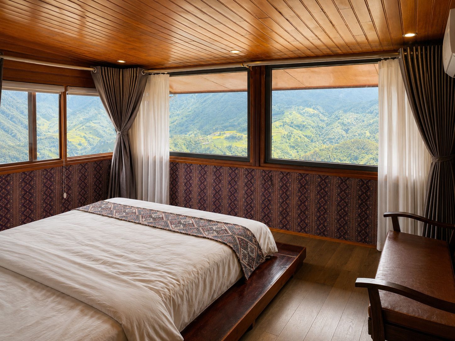 Un dormitorio con una cama grande, un banco de madera y vistas a un paisaje montañoso a través de amplios ventanales.