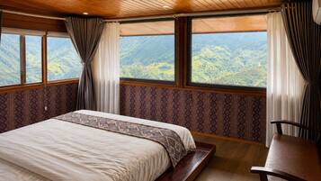 Un dormitorio con una cama grande, un banco de madera y vistas a un paisaje montañoso a través de amplios ventanales.
