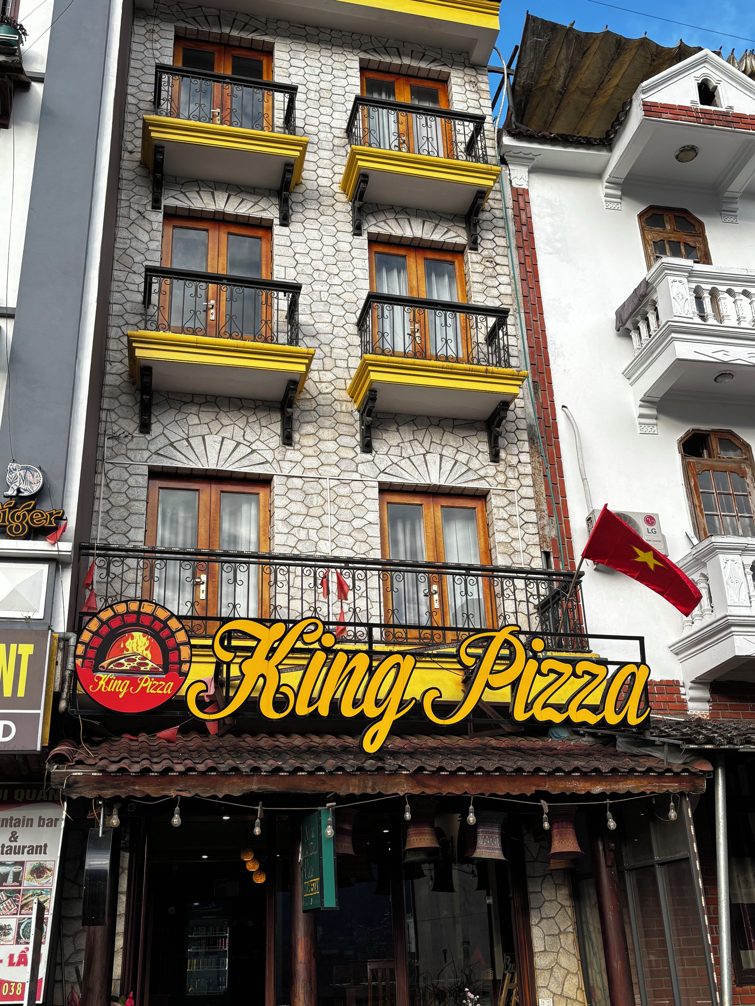 Een gebouw met een pizzeria, meerdere balkons en een vlag.