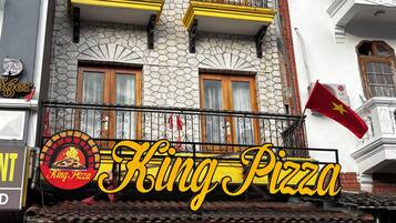 Een gebouw met een pizzeria, meerdere balkons en een vlag.