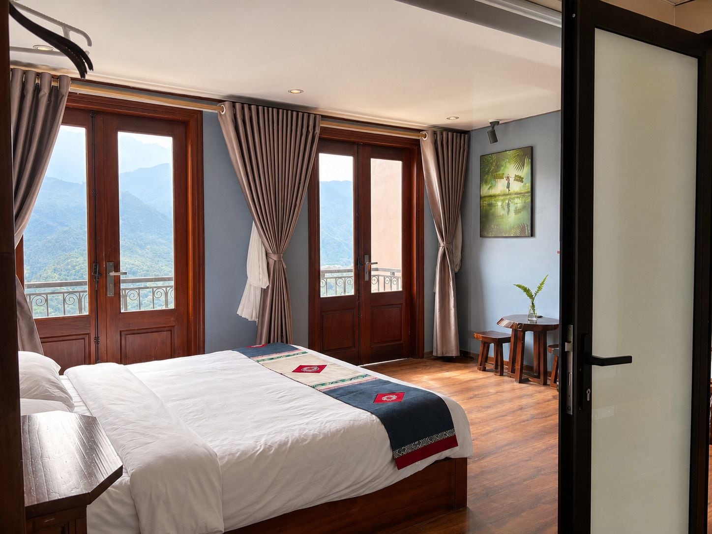 Ein Hotelzimmer mit Bett, Vorhängen, einem kleinen Tisch mit Pflanze und einem Gemälde an der Wand.