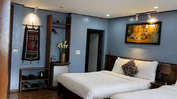 A hotel room with two beds, a wooden floor, a wall-mounted shelf with shoes, a painting, and a door.