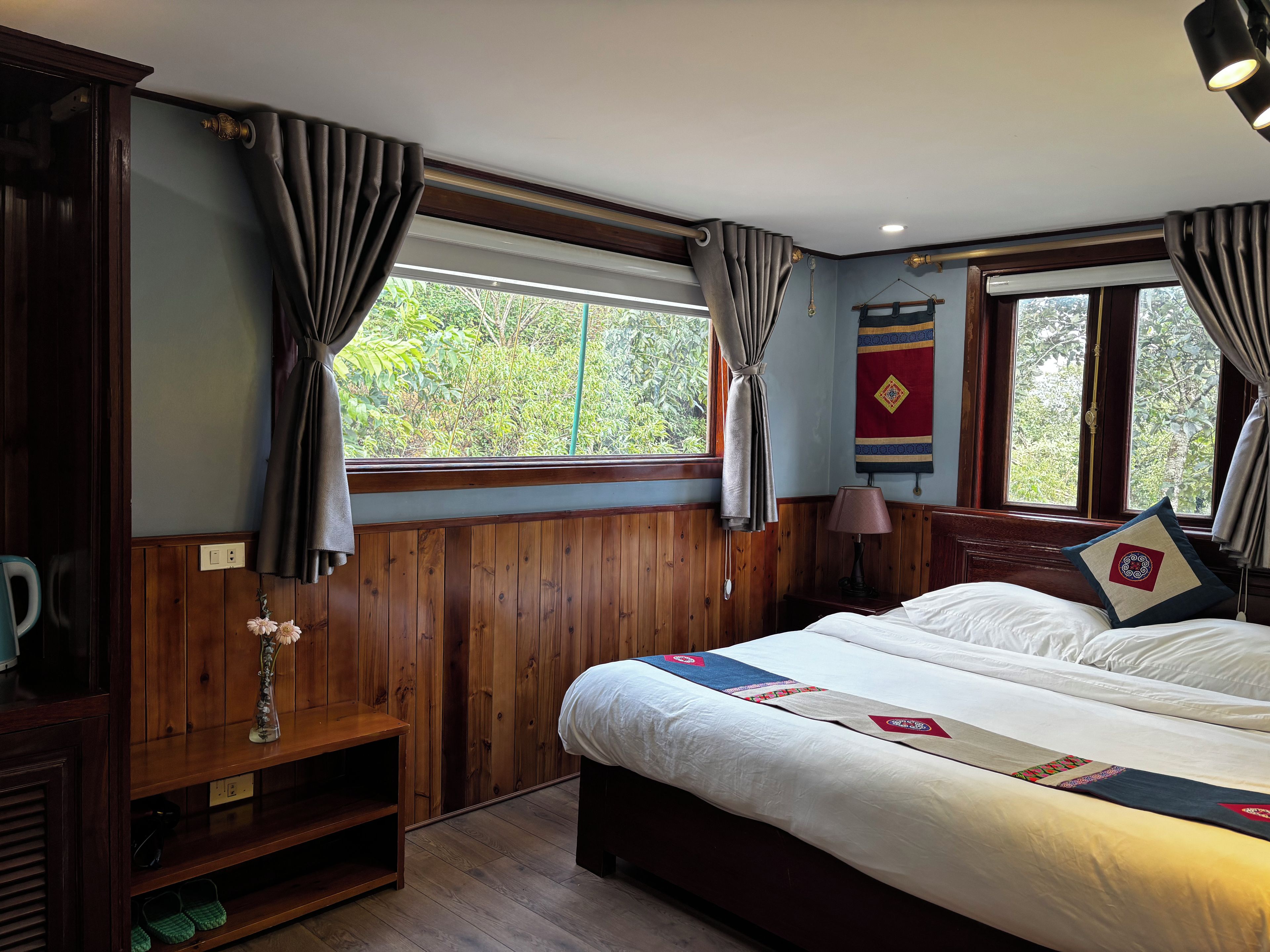 Ein Zimmer mit einem Bett, Holzwandverkleidung, einem Fenster mit Vorhängen, einer Lampe und einer Wanddekoration.