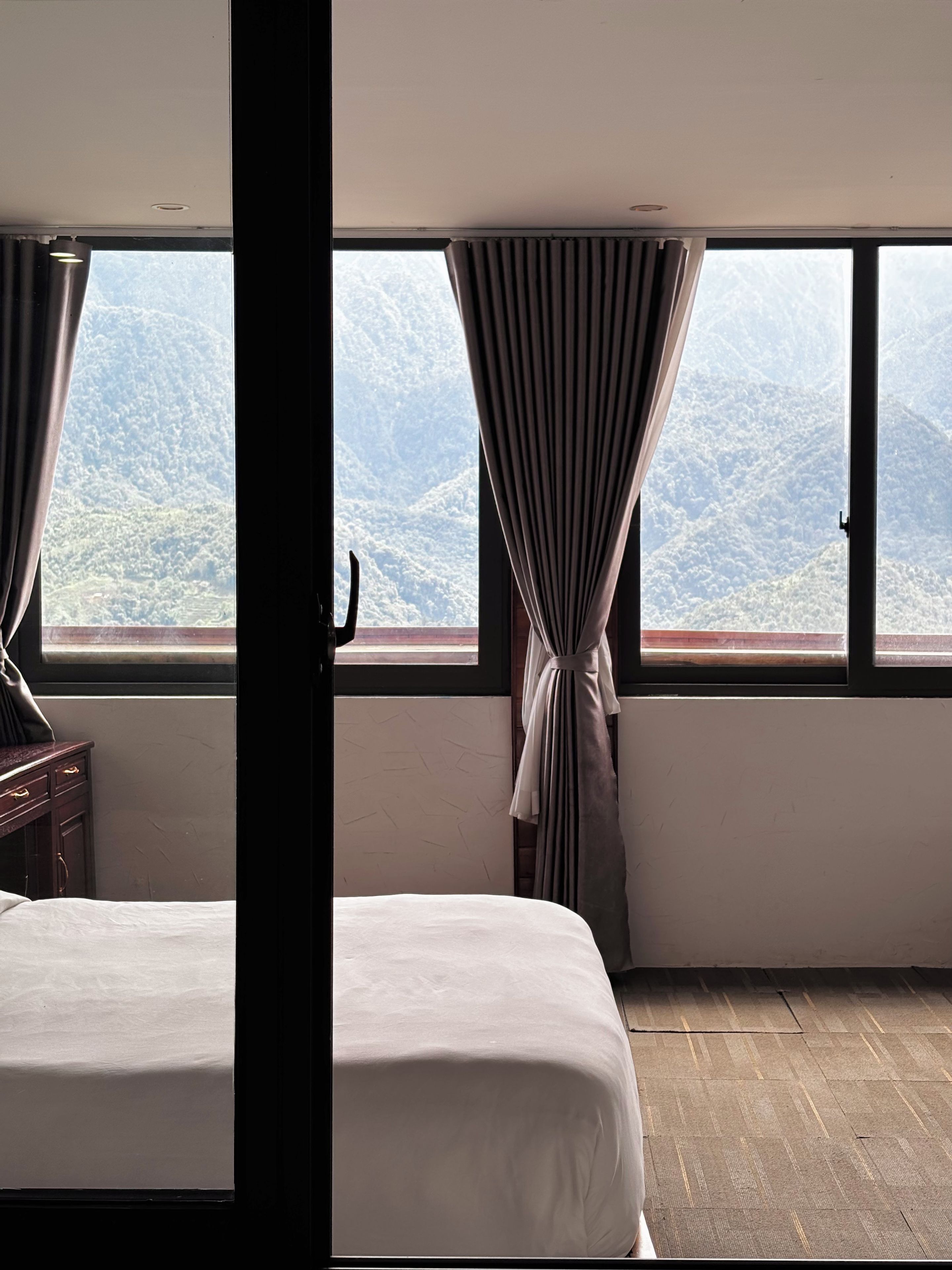 A hotel room with two beds, a view of a mountainous landscape, and a window with curtains.
