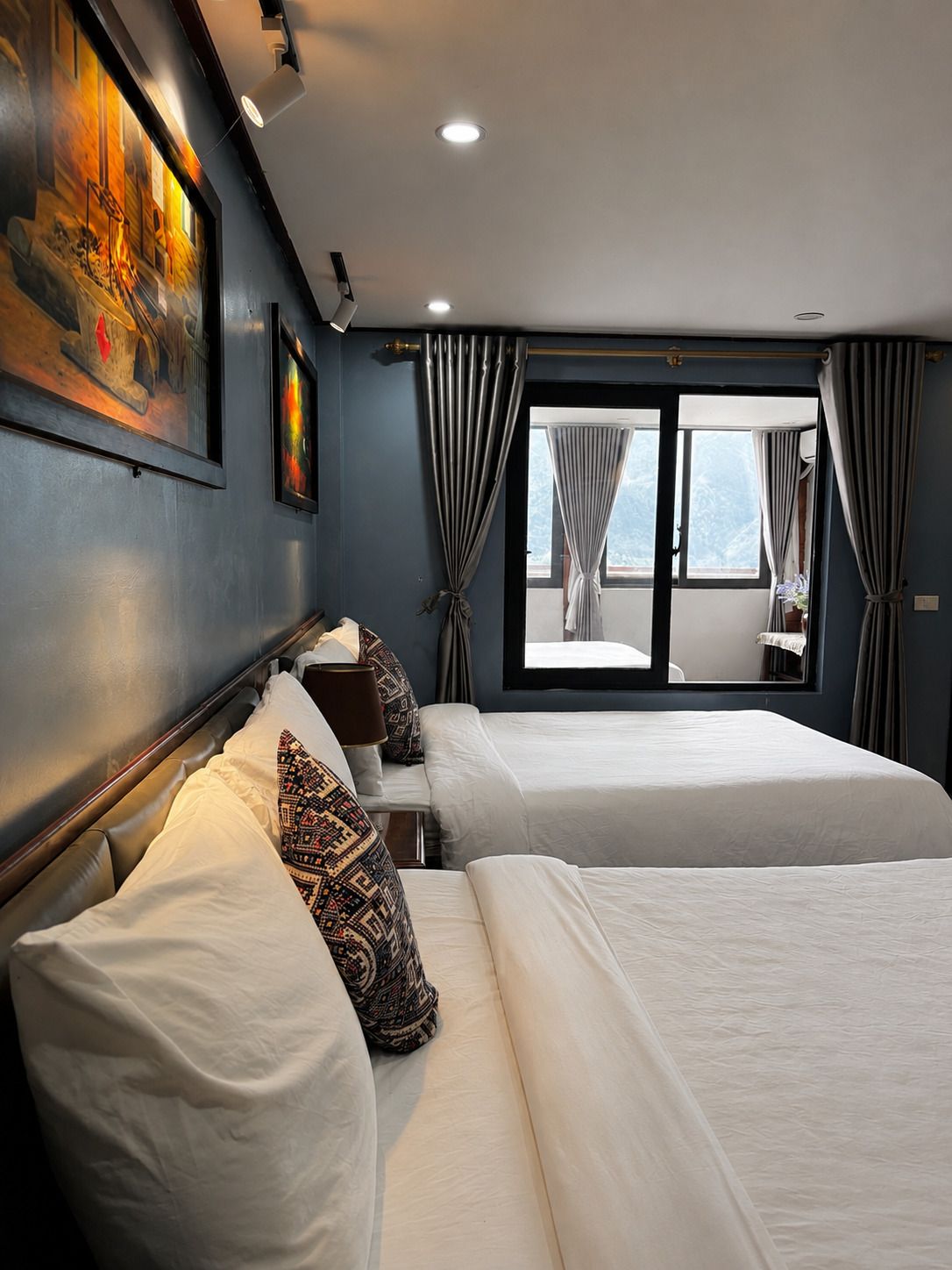 Habitación de hotel con dos camas, un ventanal con cortinas y una obra de arte en la pared.