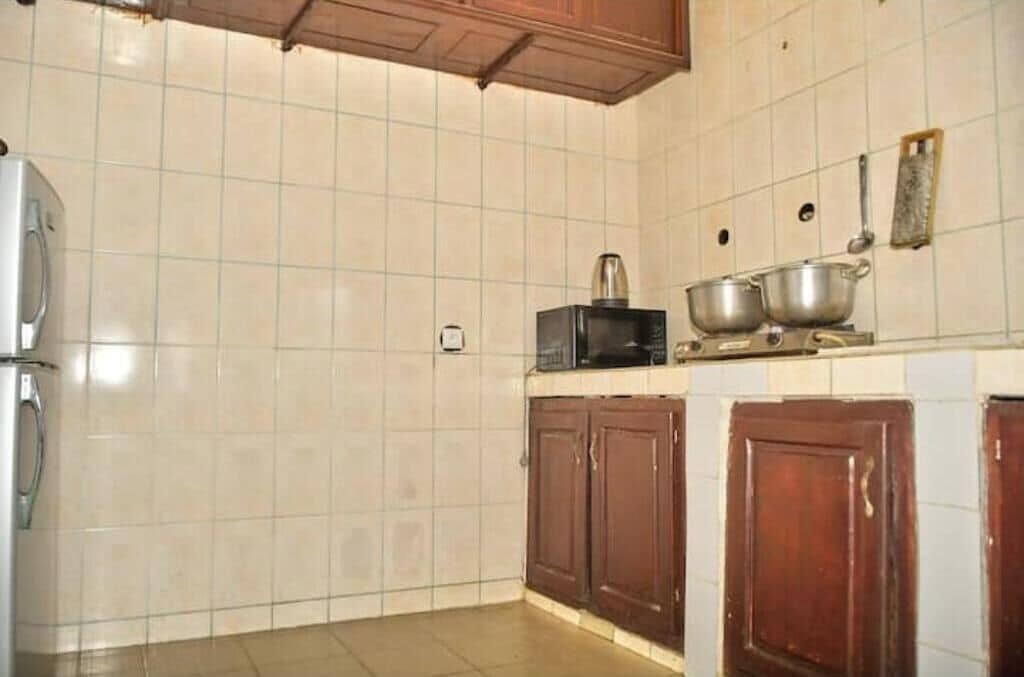 A kitchen with white tiled walls, a refrigerator, wooden cabinets, and a microwave.