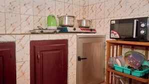 A kitchen with a microwave, pots, a green kettle, and a shelf with dishes. - NAL-Facing Apartment with Air Conditioning (Région du Littoral)